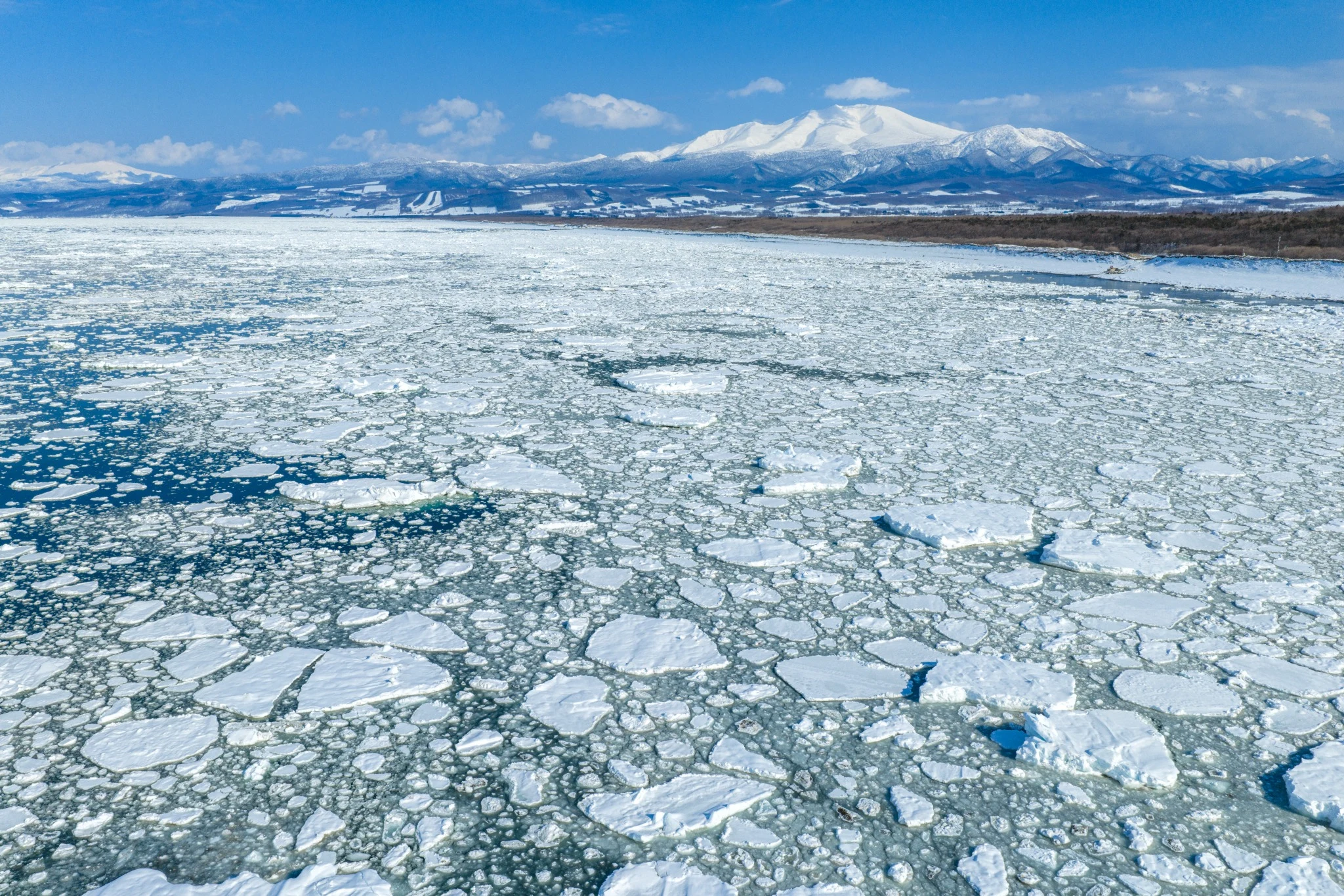 Aerial view of drift ice stretching towards the snowy Shiretoko mountains
